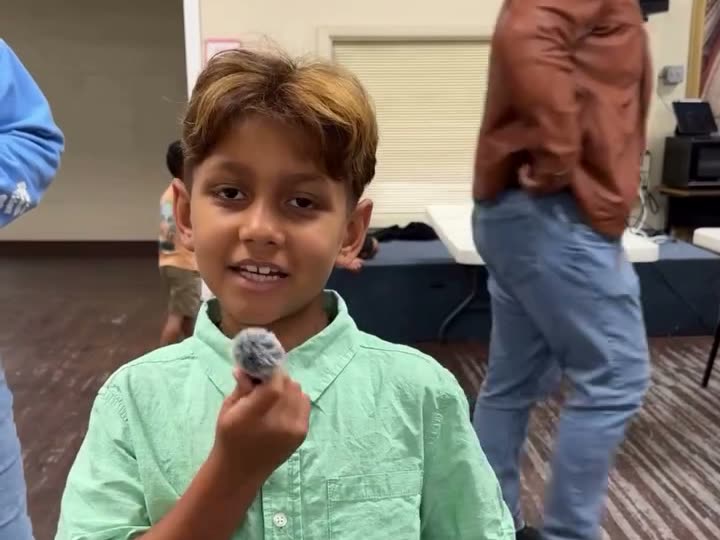 A smiling boy in a green shirt holding up a small snack