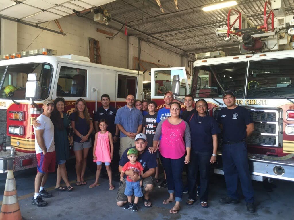 A group of adults and children posing in front of fire trucks at a fire station