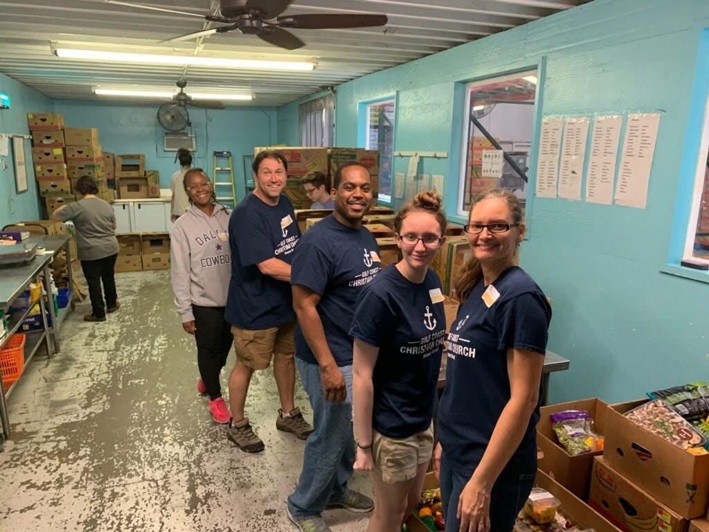 Volunteers in navy church shirts smiling in a food pantry storeroom