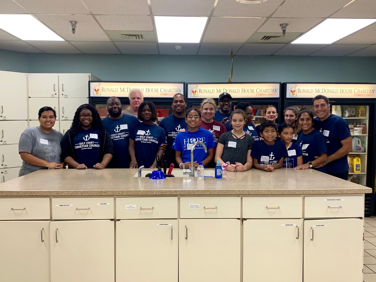 A large group of volunteers in matching navy shirts standing behind a kitchen counter